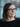 Woman with glasses smiling gently, with a blurred background.