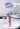 A hand in a blue medical glove pours pink liquid from a beaker into a long test tube.