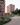 An exterior visualization of a modern residential complex with distinctive pinkish-terracotta balconies. This photorealistic visualization features a cyclist on a winding path, green lawns, and blooming spring trees.