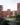Elevated exterior visualization of a modern residential neighborhood development. The 3D render displays terracotta-colored apartment buildings surrounding a green courtyard park with blooming trees.