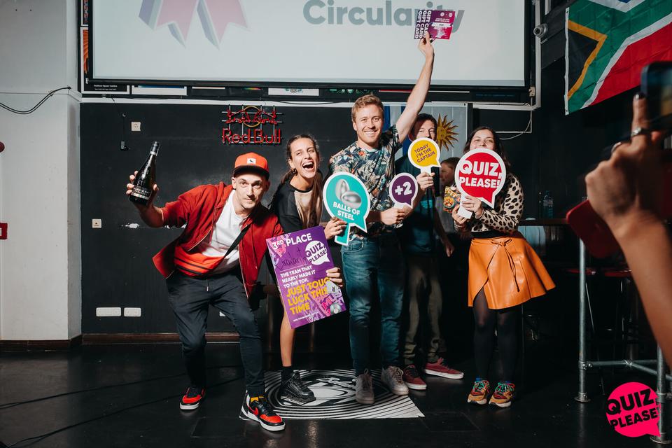 A winning team posing with Quiz, please! props and the first-place plaque