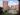 An exterior visualization showcasing an aerial view of a modern apartment complex courtyard. This photorealistic visualization captures multiple terracotta high-rise buildings, a circular canopy seating area, a playground, and lush green lawns.