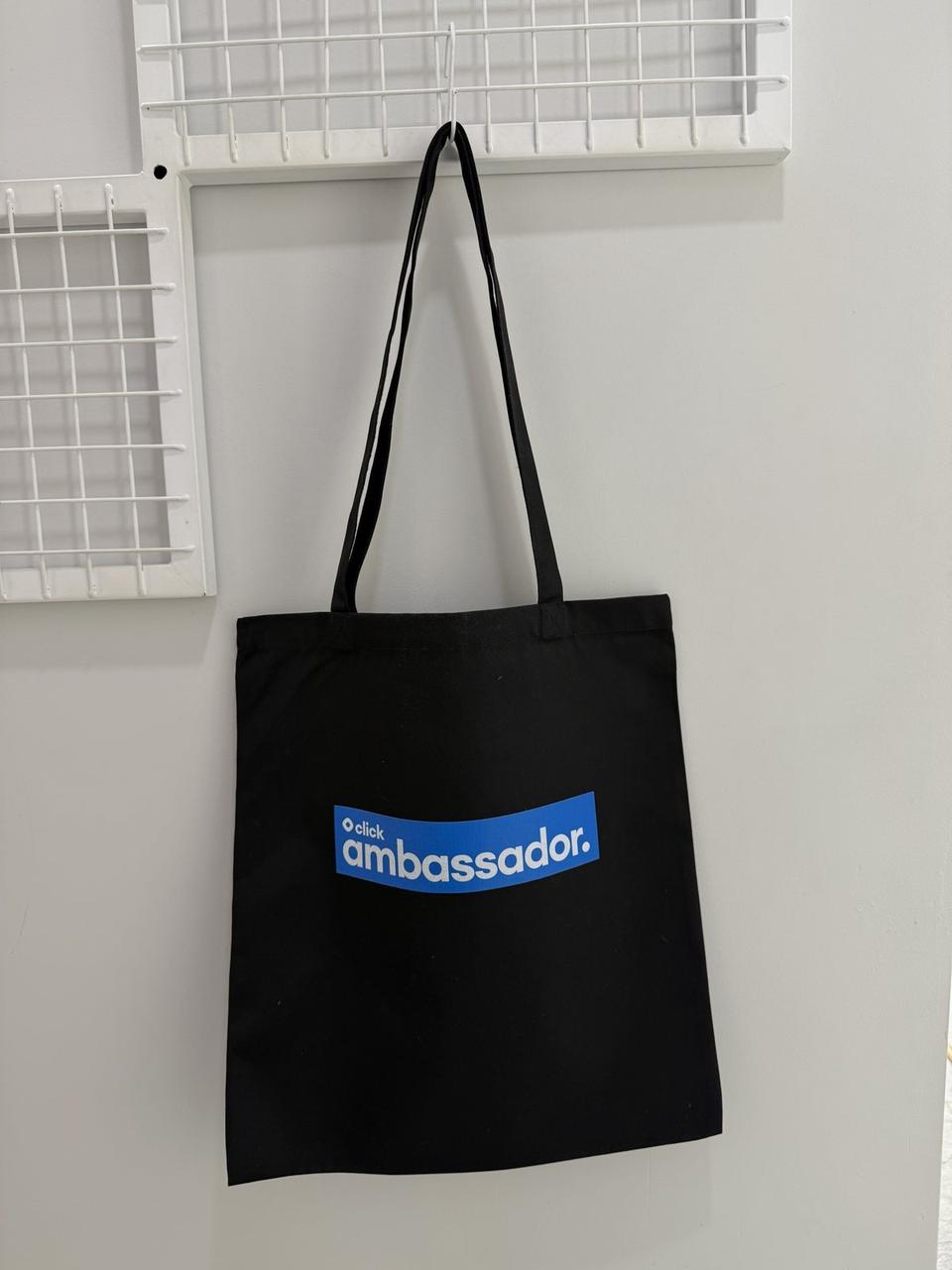 Black tote bag with a click ambassador print on a hook