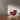 Minimalist room featuring a red accent lounge chair on a wooden herringbone floor, soft daylight, and empty framed wall art.