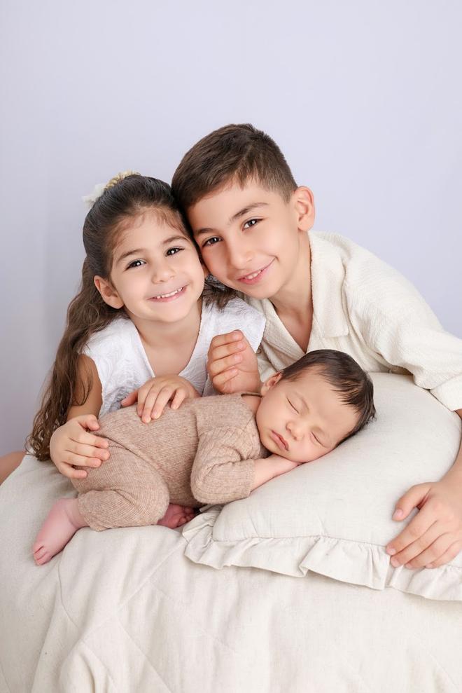 אח ואחות גדולים מחזיקים את התינוק החדש על המיטה