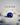 Luster – round brilliant-cut navy-blue gemstone on ivory sand with smooth pebbles, Triple L Collection
