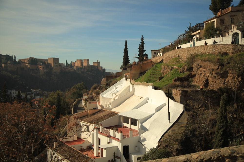 Steep hillside streets and white houses in Granada with the Alhambra behind