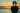 A teenage boy standing by the sea at sunset, looking down at his phone