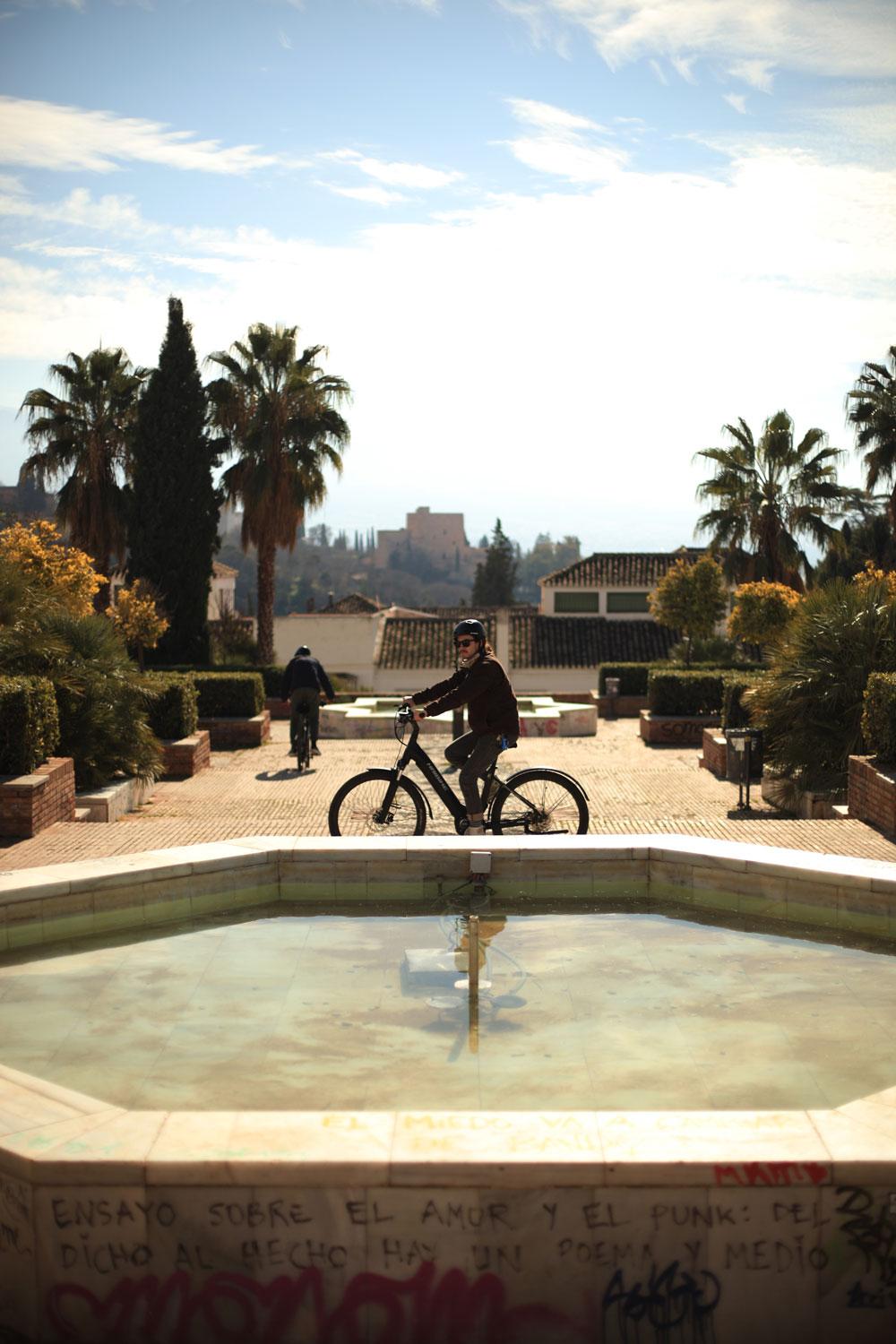 E-bike rider in a garden with a fountain and palm trees on the Alhambra hill, Granada