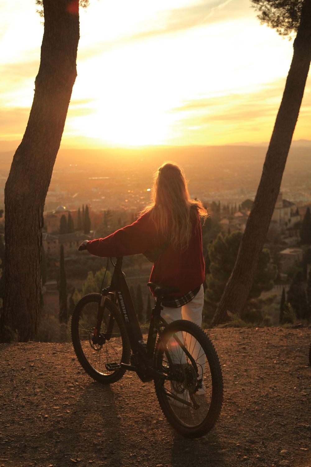 Woman with an e-bike watching the sunset over Granada from a viewpoint