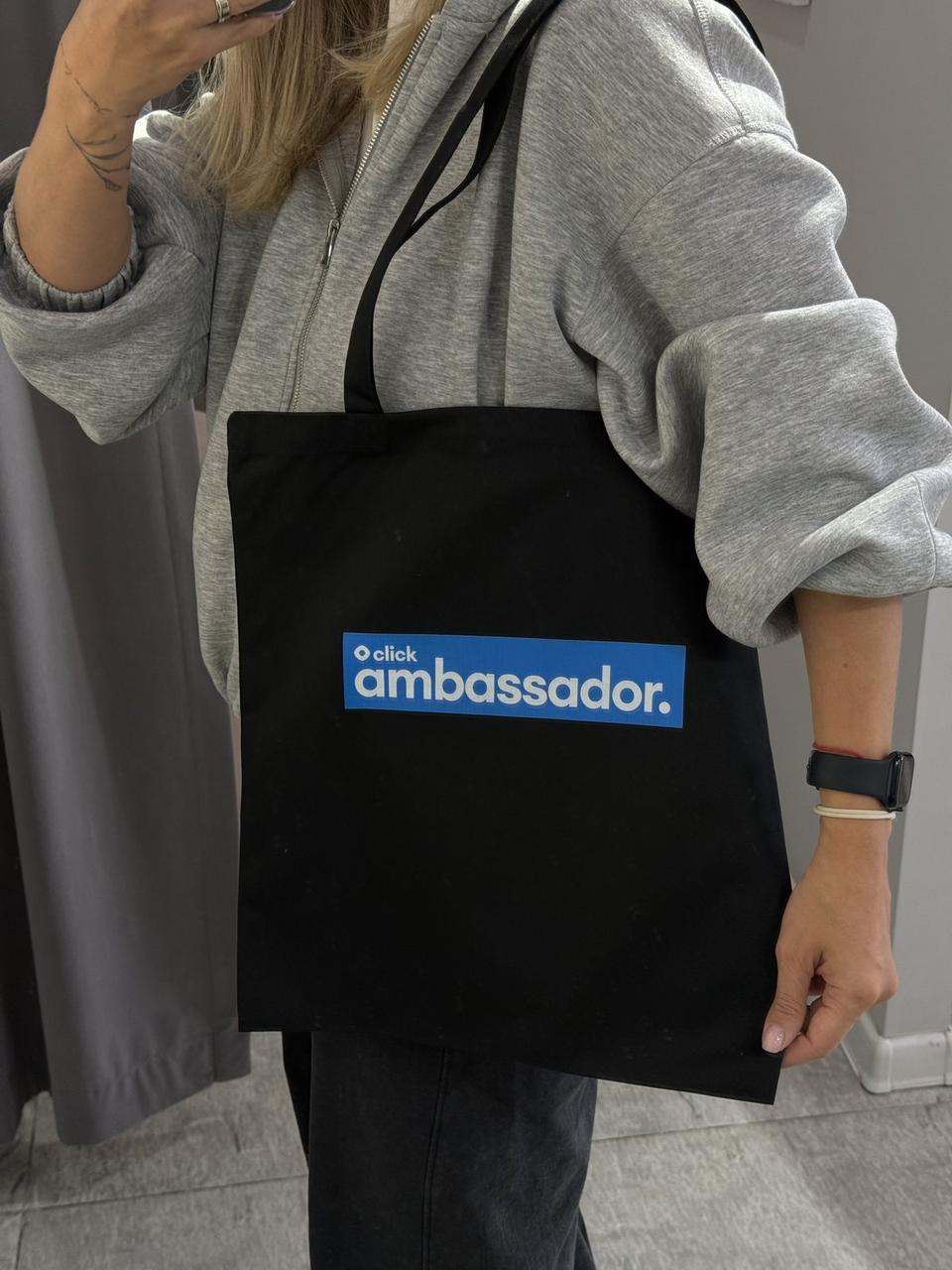 Чёрный шоппер click ambassador в руке, видно размер сумки