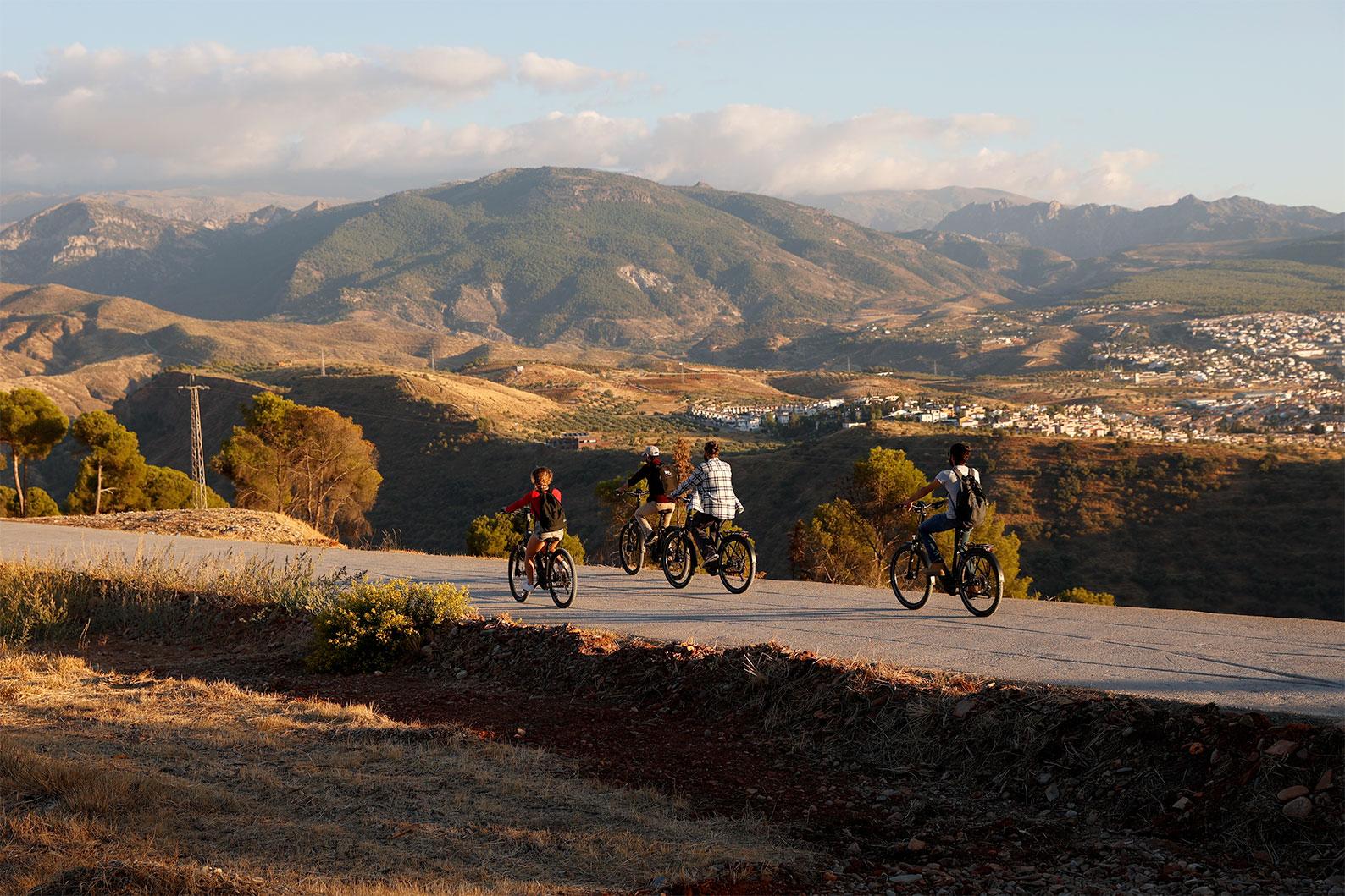 Group of cyclists on e-bikes riding a mountain road above Granada with the Sierra Nevada foothills behind